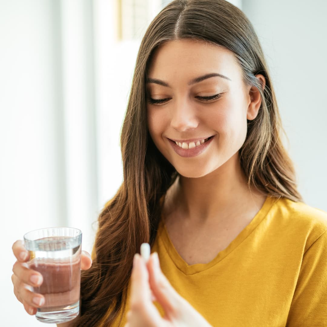 Una mujer con una pastilla y un vaso de agua en sus manos. Alimentación en madres lactantes